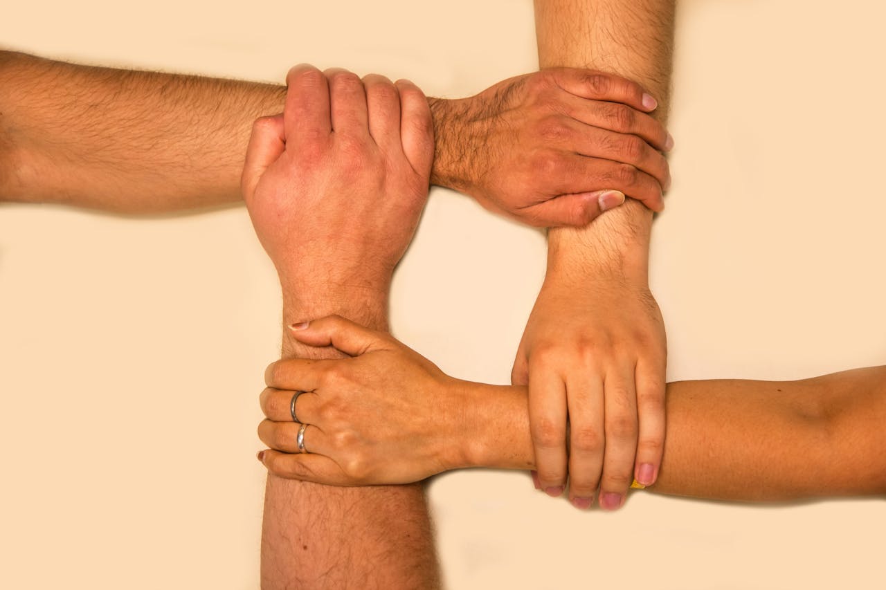 Four hands interlocked, representing unity and teamwork in a symbolic gesture.